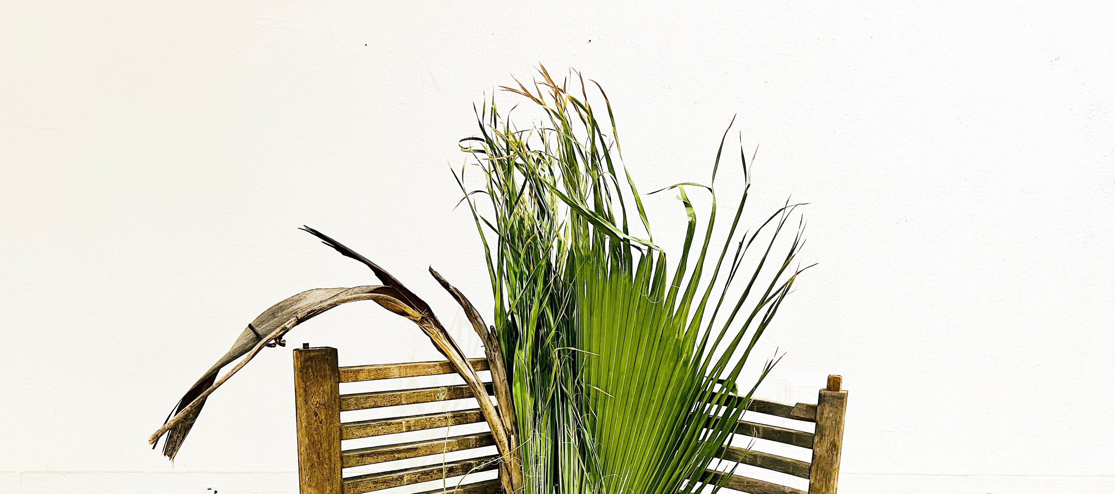 Palm leaves leaning against a wooden fence on a tiled floor.
